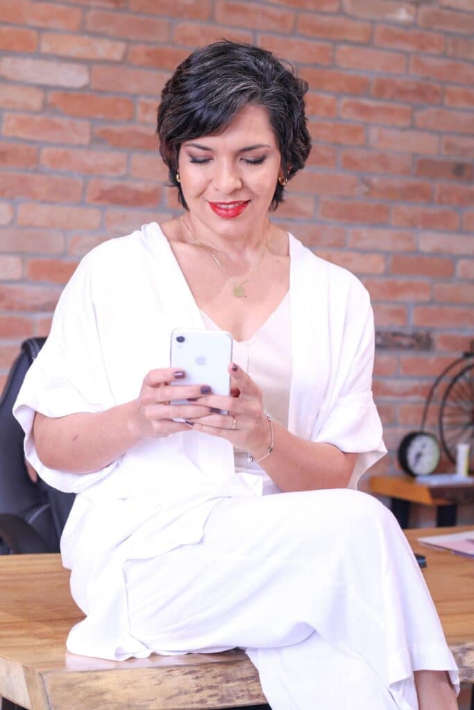Mujer sentada frente a un escritorio revisando su teléfono, esperando noticias de clientes