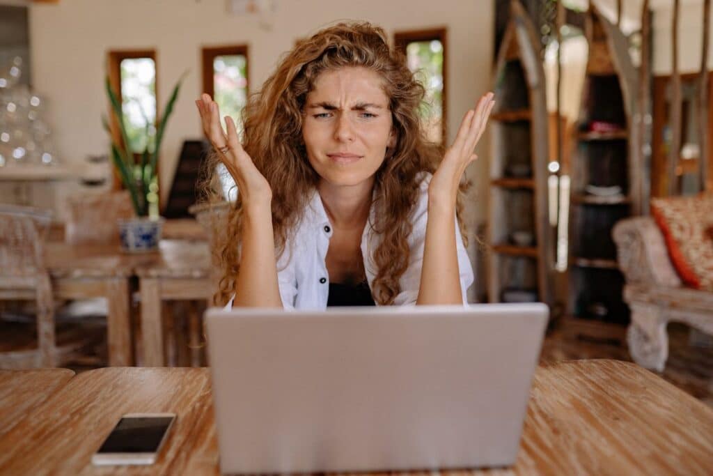 Mujer frente a su laptop con gesto de frustración y las manos levantadas