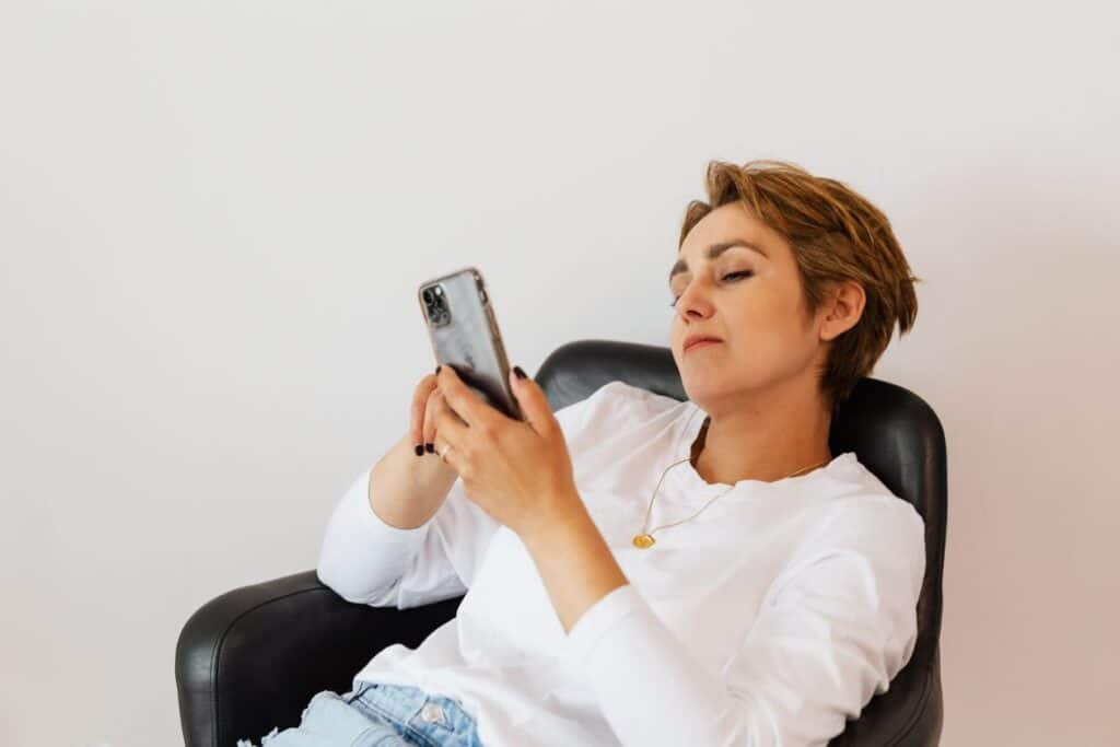 Mujer mirando el teléfono con expresión triste, comparándose con lo que ve en redes sociales